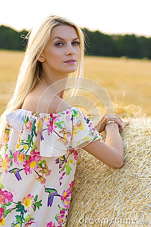 Vertical closeup portrait of a young blonde near a haystack on a background of nature, sky and field Stock Photo