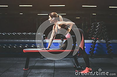 Slim, bodybuilder girl, lifts heavy dumbbell while training in the gym. Stock Photo