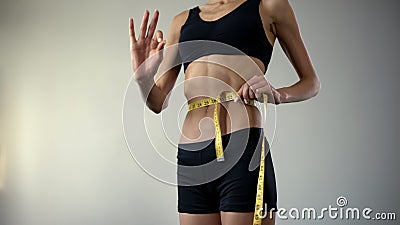 Slim girl measuring waist with tape-line, showing ok, anorexia as mental illness Stock Photo