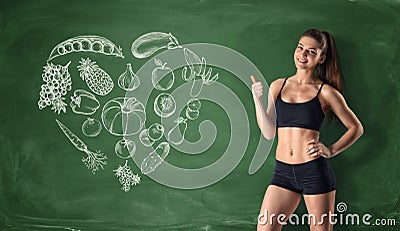 Slim girl showing thumb up on the background of painted fruits and vegetables. Stock Photo