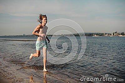 Slim long-haired man running along the river Stock Photo