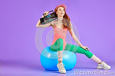 Slim student girl sits on fit ball with portable cassette player waiting to start the retro 80s dance party Stock Photo
