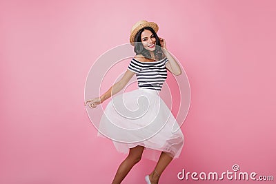 Slim stylish latin lady in hat dancing on pastel background. Cheerful tanned girl in lush skirt foo Stock Photo