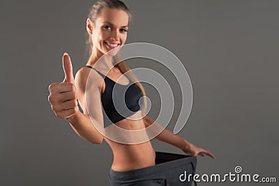 Slim young woman wearing old big pants, showing successful result of a diet - weight loss, slimming concept. gray background Stock Photo