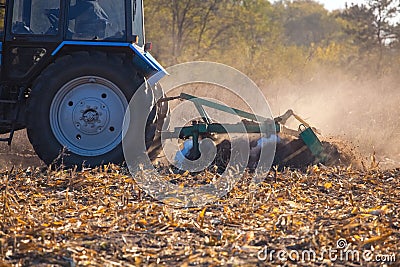 The sloping field. Big blue tractor plow plow the land after harvesting the maize crop on a autumn day. Stock Photo