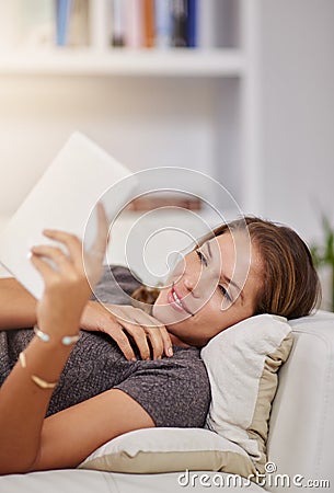 Slowing things down with an online story. a young woman relaxing on the sofa with a digital tablet at home. Stock Photo