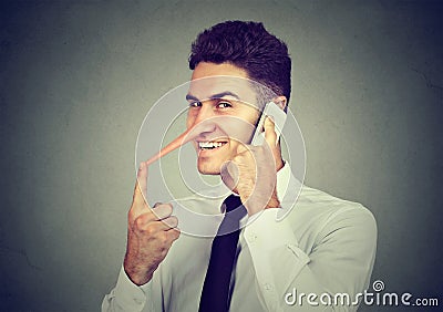 Sly young man with long nose talking on mobile phone on gray wall background. Liar concept. Stock Photo