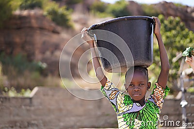 Small African Girl Returning Home From The Village Borehole With a Huge Water Bucket Stock Photo
