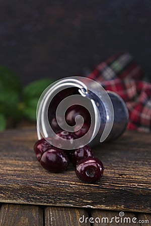 A small aluminum bucket with fresh organic red cherry fruits scattered on a wooden old textured board against a checkered red-gree Stock Photo