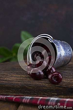 A small aluminum bucket with fresh organic red cherry fruits scattered on a wooden old textured board. Stock Photo