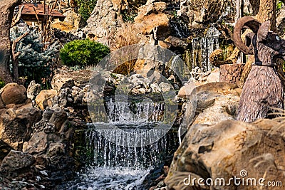 A small artificial freshwater waterfall that flows into a common Living pond. Plot structure with green moss and vegetation. Stock Photo