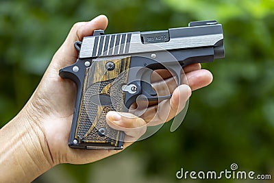 Small automatic handgun or conceal pistol in her hand on green nature background Stock Photo
