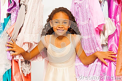 Small beautiful African girl stands among clothes Stock Photo