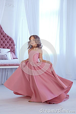 A small, beautiful girl in a luxurious pink dress, is gaily circling in a white room. Stock Photo