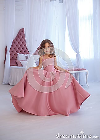 A small, beautiful girl in a luxurious pink dress, is gaily circling in a white room. Stock Photo