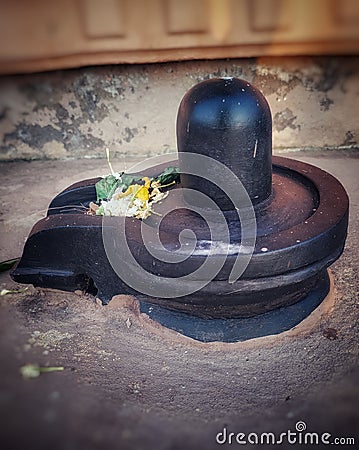 A small, black shiva-lingam made from stone and covered in flowers and bel leaves. Stock Photo