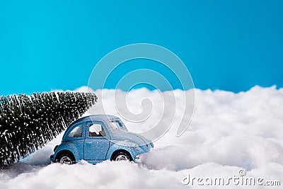 Small blue toy car carrying fir green tree for christmas party celebration drive snowy road under blue sky background Stock Photo