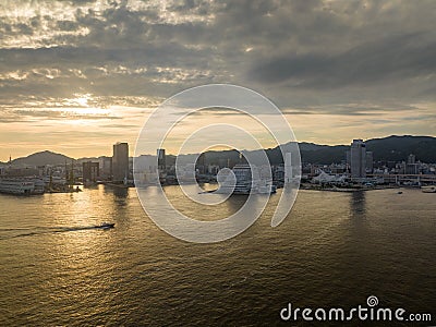 Small boat cruises toward Kobe Port and waterfront buildings at sunset Stock Photo