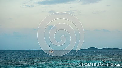 A small boat yacht sailing in the middle of sea with small island in distance as background Stock Photo