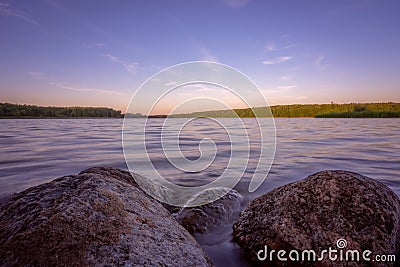 Small boulders submerged in water of a lake on a lakeshore at dusk Stock Photo