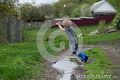 a small boy in rubber boots jumps through a muddy puddle Stock Photo