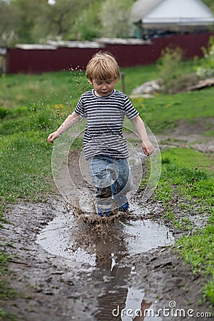 a small boy in rubber boots jumps through a muddy puddle Stock Photo