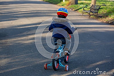 A small boy wearing a cycle helmet riding a bike in the park with stabilisers or stabilizers Stock Photo