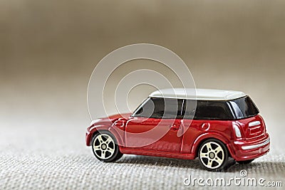 Small bright red metal simple child toy car with dark windows on light beige canvas cloth copy space background Stock Photo