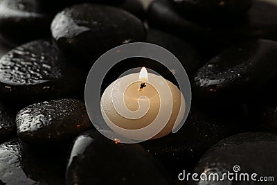 Small burning candle on wet spa stones Stock Photo