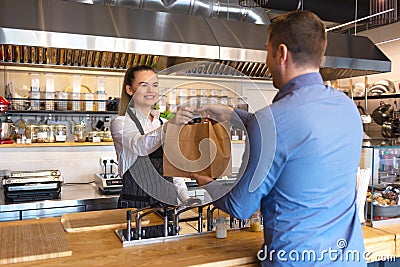 Small business and entrepreneur concept with smiling young waitress wearing black apron serving customer at counter in restaurant Stock Photo