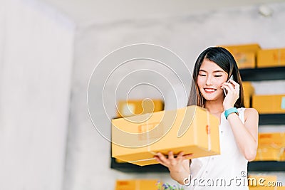 Small business owner, Asian woman hold package box, using mobile phone call receiving purchase order, working at home office Stock Photo