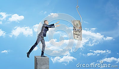 A small businessman standing on a concrete column and catching a dollar bill caught on a metal hook. Stock Photo