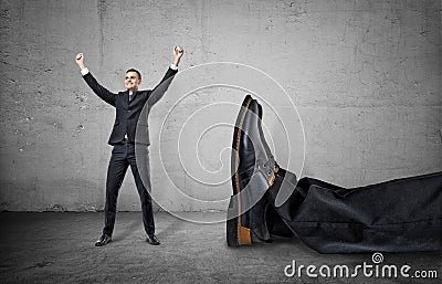 Small businessman standing with his arms up near giant leg of another man Stock Photo