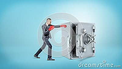 A small businessman wears red boxing gloves and hits a large broken metal safe. Stock Photo