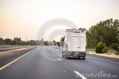 Small cargo mini van with ladder on the roof driving on the road to point of the service Stock Photo