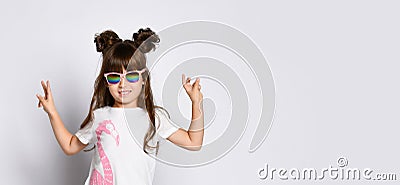 A small cheerful girl, in dark glasses in a White Studio. Stands with his hands raised and shows the peace gesture. Stock Photo