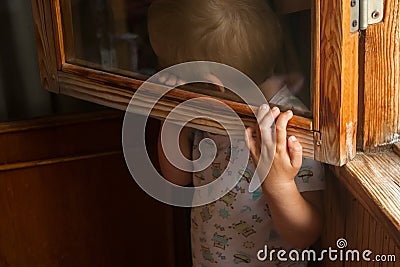 A small child is afraid of punishment and hides behind a window frame Stock Photo