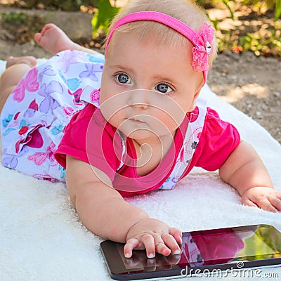 A small child lying on her stomach, playing with a tablet Stock Photo