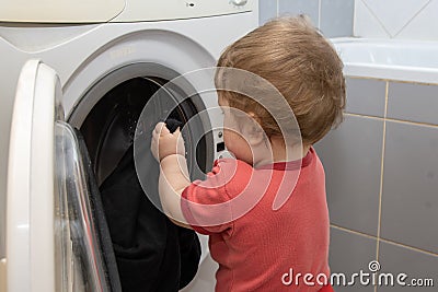 A small child pulls things out of the washing machine, a young assistant Stock Photo