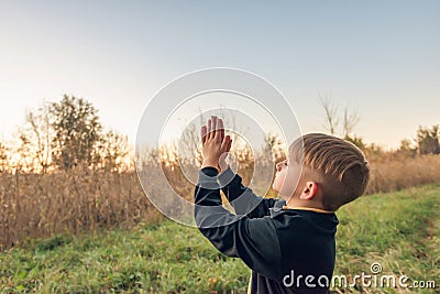A small child raises his hands to the sky, bowing in prayer in the evening park Stock Photo