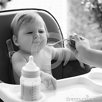 small child sits on a chair and eating with spoon. little smiling girl sits in baby-chair and have a breakfast Stock Photo