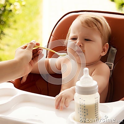 small child sits on a chair and eating with spoon. little smiling girl sits in baby-chair and have a breakfast Stock Photo