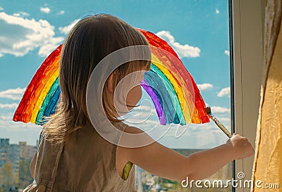 A small child stands on the windowsill and draws a rainbow on the window glass. multi-colored rainbow. symbol of happiness. select Stock Photo