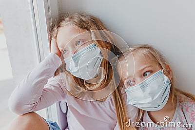 Small children in masks from coronavirus remained at home and look out the window. children are sad covid Stock Photo