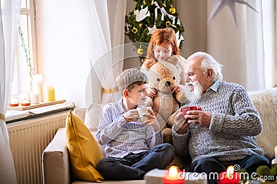 Small children with senior grandfather indoors at home at Christmas, sitting and talking. Stock Photo