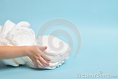 Small children& x27;s hands grab a stack of disposable diapers-panties on a light blue background. A place to copy. Stock Photo