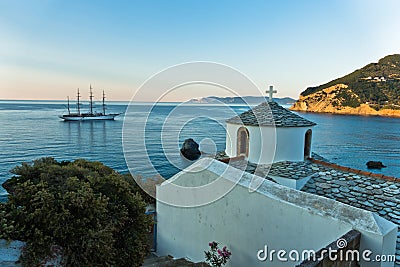 Small church and sailing ship at sunset in front of city harbor, Skopelos island Stock Photo