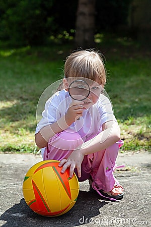 Small clever happy girl, child looking through a magnifying glass, kid with a loupe and a basketball playing in the garden outside Stock Photo