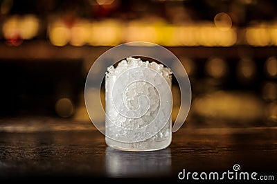 Small cocktail glass with ice pieces on the bar counter in the background of golden lights Stock Photo