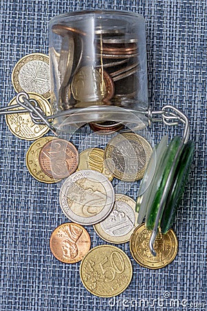 Small coins in euro cents are poured out of a glass jar on a textured blue background, selective focus, top view. A concept for bu Stock Photo